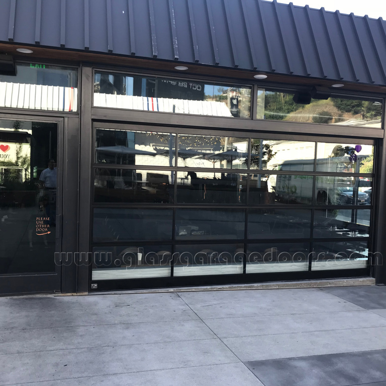 dark frame and clear glass garage door storefront with brick wall to the right 